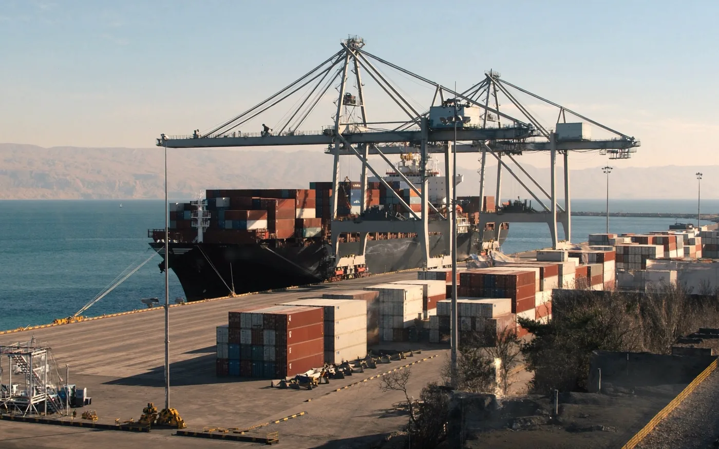 Containers stacked on the quay beside a ship at a sunlit port terminal